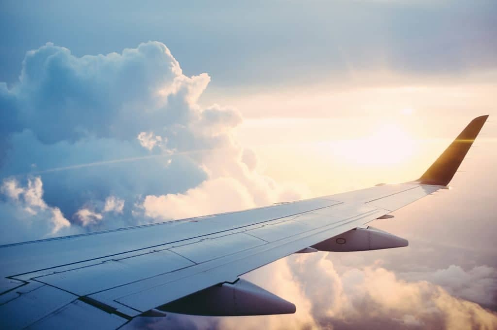 Sun peaking through clouds with a plane wing in sky