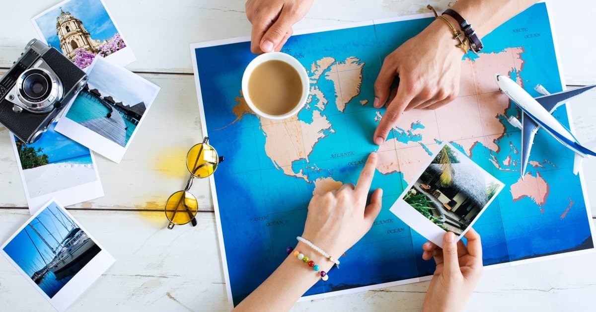 A close-up of the world map in aerial view with two people wearing bracelets and pointing at locations on the map.