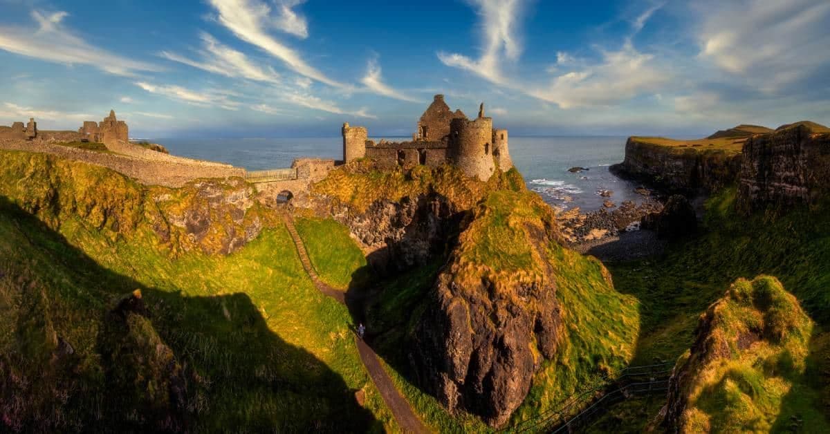 A landscape portrait of beautiful Ireland with a castle sitting cliffside. The sun is setting, highlighting the castle.