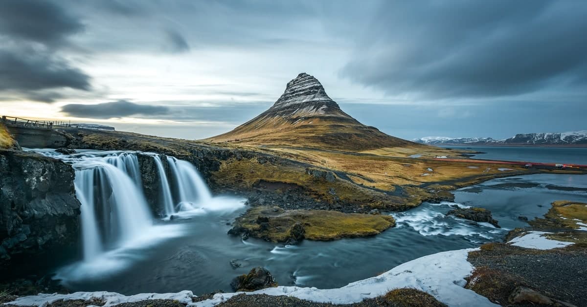 A gloomy, cloudy day in Iceland over the mountains. The waterfall drops into the base of the mountains.