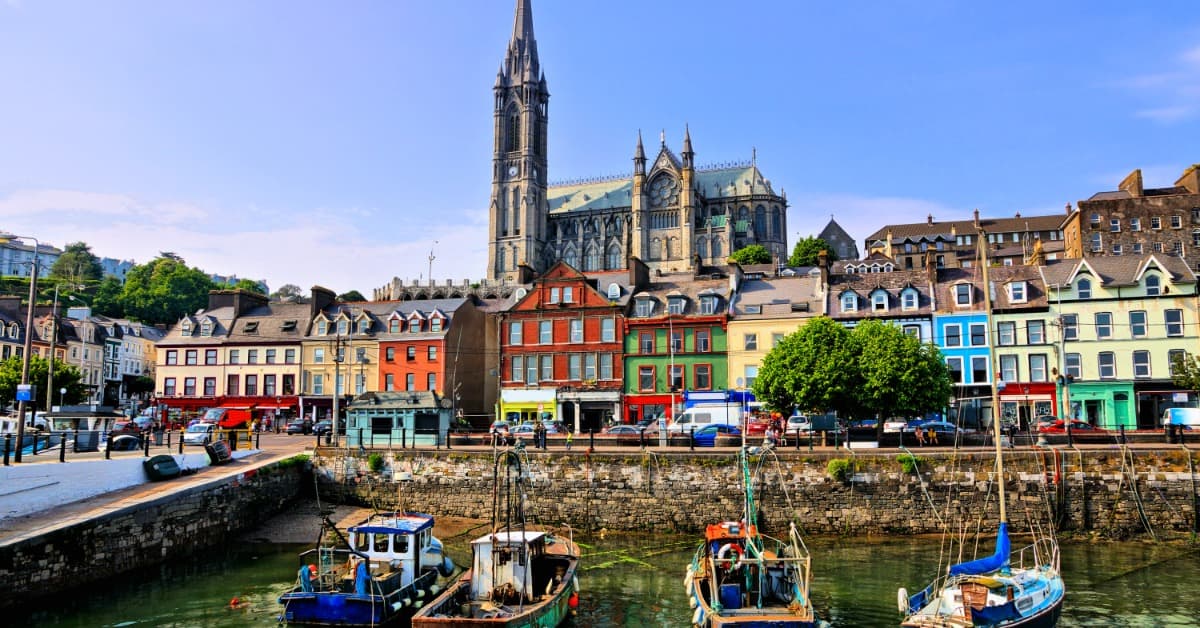 A small river town in Ireland surrounded by cobblestone roads and buildings. There are small boats docked by the bridge.